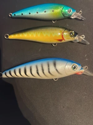 Tre färgglada fiskedrag - Säljer tre olika fiskedrag i plast med realistiska fiskmönster. Ett är blått och grönt med svarta prickar, ett är gult med röda detaljer och ett är blått och vitt med svarta ränder. 