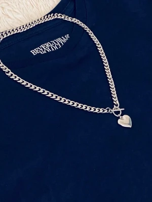 Kedjehalsband med hjärthänge - Snyggt silverfärgat halsband med grov kedja och ett hjärthänge. Halsbandet har en toggle-låsning framtill som ger en trendig touch. Perfekt accessoar för att lyfta din outfit med en cool och stilren detalj.