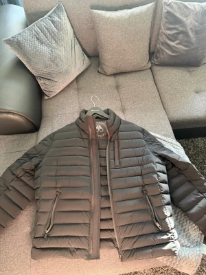 Moose Knuckles lättviktsjacka - Riktigt fin lättviktsjacka i dun från Moose Knuckles med snygga detaljer. Jackan är självklart äkta och tagg finns på  bilderna. Storlek är XL men passar både L/XL. Den är i totalt nyskick och i princip oanvänd. Säljes då den bara står i garderoben. Original galje medföljer också. Nypris ca 8000kr. Jackan är i svart färgen men solljuset gör den grå på bilden. 