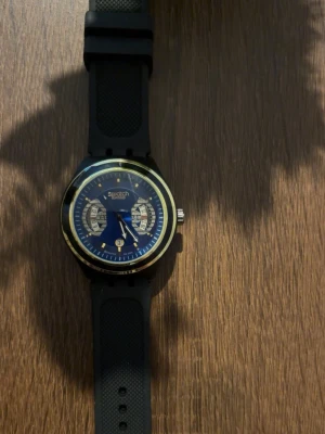 Klocka  - Snygg klocka med blå urtavla, svarta detaljer och guldfärgad ram. Klockan har svart silikonarmband med struktur och tydliga visare. Perfekt accessoar för dig som vill ha en stilren och modern look.