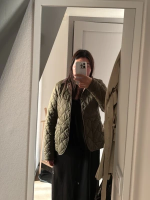 Barbour jacka - Snygg olivgrön quiltad jacka med klassiskt mönster och dragkedja framtill. Jackan har en figurnära passform och långa ärmar, perfekt för lager-på-lager under kyligare dagar. Storlek:38