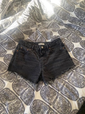 Svarta jeansshorts - Snygga svarta jeansshorts med rå, fransig kant nertill och klassisk femficksmodell. Shortsen har knapp och dragkedja framtill samt bälteshällor. Perfekta för en avslappnad stil under varma dagar. 🌸