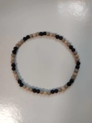 Svart/grå beige pärlhalsband - elastiskt halsband med träpärlor - Halsband med runda träpärlor i beige, grått och svart. Halsbandet är ca 42 cm och elastiskt så passar nog de flesta. Har knappt använts.