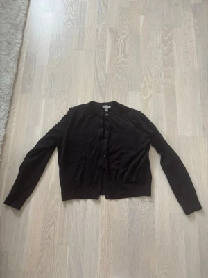 Svart kofta från H&M - En klassisk svart kofta från H&M med rund halsringning och knäppning framtill. Långärmad modell i mjukt och tunt material, perfekt att slänga över en t-shirt eller linne. Enkel och stilren design som funkar till det mesta. Storlek L men sitter mer som en M/S