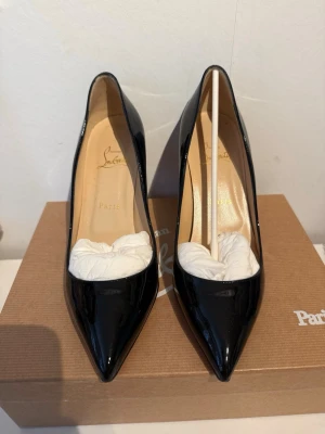 Svarta lackpumps från Christian Louboutin - Stilrena svarta pumps i lack från Christian Louboutin med spetsig tå och klassisk siluett. Skorna har en elegant och tidlös design med beige innersula och hög klack. Perfekta för dig som vill ha en lyxig och trendig look.