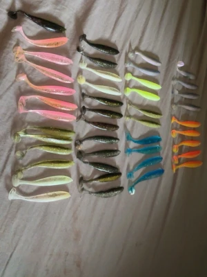 Blandade mjuka fiskedrag i olika färger - Säljer ett gäng mjuka fiskedrag i olika färger och former. Här finns drag i blått, orange, rosa, gult, vitt, grönt och silver, flera med glittereffekt. Perfekta till abborrfiske eller gädda. Tillverkade i mjuk plast och varierar i storlek och form för olika fiskesituationer.