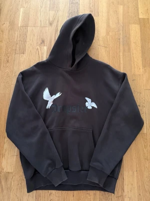 Svart hoodie med duvor och Dropsize-tryck - Svart hoodie med huva och magficka. På bröstet finns två vita duvor och texten 'Dropsize' i gotisk stil. Hoodien har ribbade muddar och är gjord i ett mjukt material som passar perfekt till en avslappnad streetwear-look.