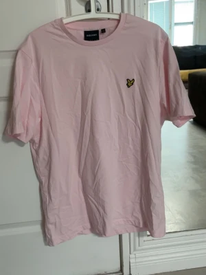 Lyle & Scott T-shirt  - Ljusrosa Lyle & Scott T-shirt i storlek Large. Tröjan har en väldigt liten fläck som syns på bild 3. Annars knappt använd 