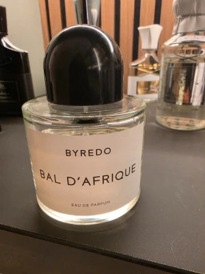 Byredo Bal d'Afrique Eau de Parfum 100ml - Byredo Bal d'Afrique Eau de Parfum i en stilren, rund glasflaska med svart kupolformat lock. Doften har en elegant och modern design med tydlig etikett framtill. Perfekt för dig som gillar exklusiva och unika parfymer.