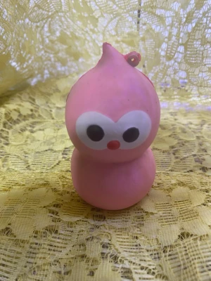 squash Rosa figur  med stora ögon - Söt rosa figur squash i mjukt med stora vita ögon och liten röd näsa. Formen är rundad med två sektioner och en liten ögla på toppen, perfekt som dekoration eller leksak. Passar att ha på skrivbordet eller som nyckelring.
