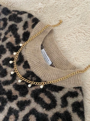 Guldhalsband med pärldetaljer - Snyggt halsband i guldfärgad metall med små vita pärlor som hänger längs kedjan. Kedjan har en klassisk, lite chunky design och pärlorna ger en elegant touch. Perfekt accessoar för att lyfta vilken outfit som helst.
