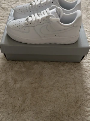 Vita sneakers Nike Air Force 1 - Klassiska helvita Nike Air Force 1 sneakers i lågt utförande. Skorna har en stilren design med perforerad tå, vita skosnören och sula i gummi. Tillverkade i läder med ikoniska swoosh-loggan på sidan. Perfekta för en clean och tidlös look. Helt nya storlek 42