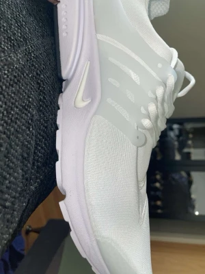 Vita Nike sneakers med mesh och plastdetaljer - Snygga vita Nike sneakers med låg profil, tillverkade i mesh och med plastdetaljer på sidan. Skon har en tydlig Swoosh-logga och vita skosnören. Perfekt för dig som gillar stilrena och sportiga skor.