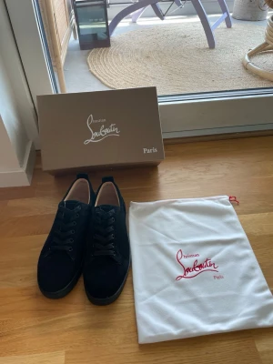 Svarta sneakers från Christian Louboutin - Stilrena svarta sneakers från Christian Louboutin i mocka med klassisk låg silhuett. Skorna har svarta snören och diskreta detaljer, samt kommer med originalkartong och dustbag med logga. Perfekta för dig som vill ha en lyxig touch på din outfit. Skriv vid minsta funderingar! Har kvitto och allt