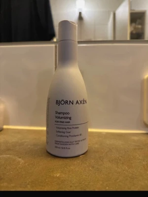 Björn Axén Volumizing Shampoo - Volymgivande schampo från Björn Axén för fint hår. Innehåller risprotein, mjukgörande socker och provitamin B5. Flaskan är vit med svart text och rymmer 250 ml. Perfekt för dig som vill ha mer fyllighet i håret.