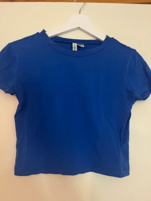 Blå basic t-shirt från H&M Divided - En enkel blå t-shirt från H&M Divided i storlek M. T-shirten har rund halsringning och korta ärmar. Tillverkad i mjuk bomull som känns skön mot huden. Perfekt till sommaren, toppen är lite cropped och har ett stretchiga material.