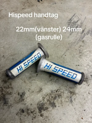 Hispeed handtag till moped - Säljer ett par Hispeed handtag för moped eller motorcykel. Ena handtaget är 22mm för vänster sida och det andra är 24mm för gasrulle. Handtagen är vita med blå text och detaljer, tillverkade i plast och gummi.