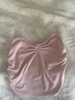 Ljusrosa linnetopp - Säljer en ljusrosa linnetopp med tunna axelband och rynkade sidor. Toppen har en lätt draperad framsida och är tillverkad i ett mjukt material som känns skönt mot huden. På lappen står det M men själv tycker jag den är S.