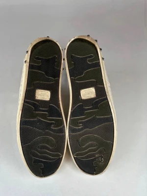  Valentino flycrews - Snygga vita sneakers från Valentino i mjukt läder med klassisk låg profil och diskreta sömdetaljer. Skorna har vita snören, beige sula och subtil logga på plösen. Perfekta för en clean och stilren look.