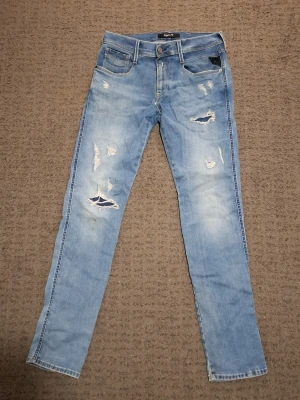 Ljusblå Replay jeans  - Säljer ett par ljusblå Replay jeans med slitningar. Jeansen har fem fickor, passform slim fit, storlek 30W 32L. Materialet är mjukt denim med stretch för extra komfort. Perfekta för en avslappnad och trendig look. Har en liten brun fläck på framsida. Köpta från Åhlens för 1500 kr