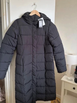 Svart lång dunjacka med huva - Säljer den populära dunjackan ifrån Lager157. Slutsåld på hemsidan. Lång dunjacka med huva och dragkedja framtill. Ny med prislapp. 