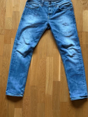 Ljusblåa dondup jeans med slitningar - Säljer ett par ljusblå jeans med raka ben och slitningar på framsidan. Klassisk femficksmodell med dragkedja och knapp. Jeansen har en avslappnad tvätt och är tillverkade i denim. Perfekta för en casual look.