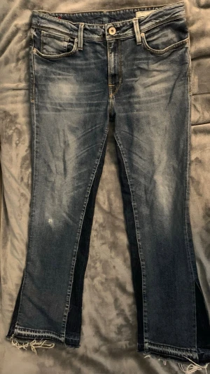 Blå flared jeans  - Säljer ett par blå jeans från Bershka med slitningar och råa, fransiga benslut. Jeansen har klassisk femficksmodell, normalhög midja och lätt utsvängda ben. Materialet är denim i bomull med stretch. Perfekta för en avslappnad och trendig look.