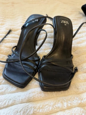 Svarta strappy sandaler från Zara - Säljer ett par svarta sandaler från Zara med tunna remmar och fyrkantig tå. Klackarna är höga och smala, och sandalerna har långa snörningar som kan lindas runt ankeln. Har använt en gång. Vid frågor skriv 💬 