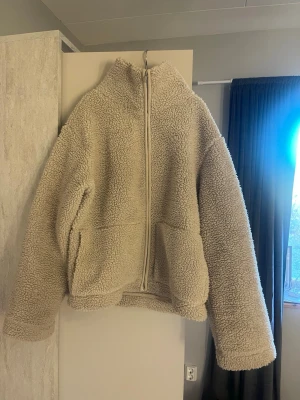 Beige teddyjacka med dragkedja - Mysig beige teddyjacka med hög krage och hel dragkedja framtill. Jackan har två stora fickor och oversized passform för en avslappnad look. Perfekt för kalla dagar när du vill vara både varm och trendig. Andvänd några gånger men inga defekter💕