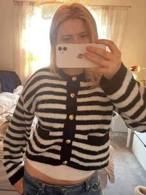 Svartvit randig kofta med guldknappar - Cool svartvit kofta med breda ränder och snygga guldknappar framtill. Koftan har två små fickor och är gjord i ett fluffigt, mjukt material.🤗