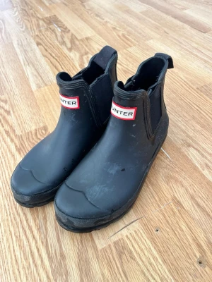 Svarta gummistövlar från Hunter - Säljer ett par svarta, klassiska gummistövlar från Hunter. Modellen är ankelhög med elastiska paneler på sidorna.