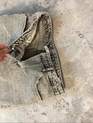 Grå tvättade raka jeans från Zara - Säljer ett par grå tvättade jeans från Zara med rak passform och klassisk femficksdesign. Jeansen har hög midja och stängs med knapp och dragkedja. Materialet är kraftig denim i bomull och färgen har en snygg vintagekänsla.