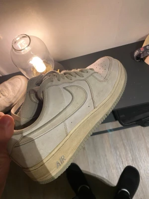 Nike Air Force 1 vita sneakers - Klassiska vita Nike Air Force 1 sneakers med låg profil och ikonisk swoosh på sidan. Skorna har perforerad tåbox för ventilation, snörning och en kraftig sula med AIR-dämpning. Tillverkade i läder med textildetaljer. Perfekta för en clean och tidlös streetstil.