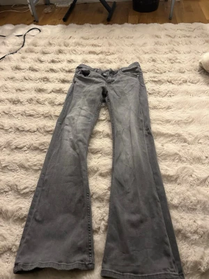 Grå bootcut jeans med utsvängda ben - Säljer ett par gråa bootcut jeans med utsvängda ben och klassisk femficksmodell. Jeansen har normal midja och dragkedja med knapp framtill. Perfekta för dig som gillar en avslappnad men ändå trendig look.