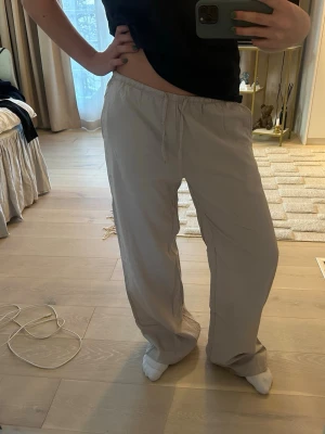 Beiga linnebyxor från 157 - Säljer ett par beiga linnebyxor från 157 med avslappnad passform och resår i midjan med dragsko. Byxorna är raka i modellen och tillverkade i ett tunt, luftigt material som passar perfekt för en chill och stilren look.