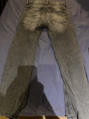Grå tvättade raka jeans - Säljer ett par grå tvättade jeans med raka ben och klassisk femficksmodell. Jeansen har en snygg slitning på låren och baksidan, samt normal midja. Perfekta för en avslappnad och trendig look. Materialet är denim i bomull.
