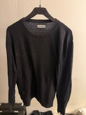 Svart tröja från Jack & Jones - En enkel och stilren svart tröja från Jack & Jones. Tröjan har rund halsringning, långa ärmar och ribbade muddar vid ärmslut och nederkant. Perfekt basplagg i garderoben och lätt att matcha med olika outfits.