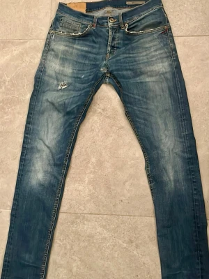 Blå slim fit jeans med slitningar - Snygga blå slim fit jeans med slitningar och ljusa tvättade partier på benen. Klassisk femficksmodell med knappgylf och kontrastsömmar. Perfekta för en avslappnad och trendig stil.