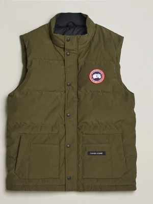 väst från Canada Goose - Snygg olivgrön dunväst från Canada Goose med hög krage, tryckknappar och två stora framfickor. Västen har det klassiska Canada Goose-märket på bröstet och är vadderad för extra värme. Perfekt att slänga över en hoodie eller tröja för en chill look.