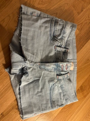  jeansshorts - Säljer ett par ljusblå jeansshorts från Nelly med råa, fransiga kanter och klassisk femficksdesign. Baksidan har två fickor med rosa sicksack-broderier. Perfekta för varma dagar och en avslappnad stil. HELT oanvända pga fel storlek ❤️