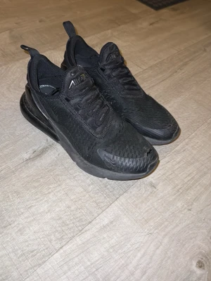 Nike Air Max 270 helsvarta sneakers - Säljer ett par helsvarta Nike Air Max 270 sneakers med mesh-ovandel och synlig Air-enhet i hälen. Skorna har en sportig siluett, rund tå och klassiska Nike-detaljer på plösen och sidan. Perfekta för dig som gillar streetwear och bekväma skor.