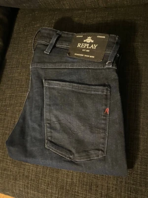 Mörkblå jeans från Replay - Snygga mörkblå jeans från Replay med klassisk femficksmodell och diskret röd detalj på bakfickan. Jeansen har slim fit ben och är tillverkade i ett mjukt denimtyg som ger en skön passform. Perfekta för dig som gillar stilrena och tidlösa jeans.
