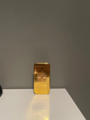 Paco Rabanne 1 Million Parfym (1/2 kvar) - Säljer en Paco Rabanne 1 Million parfym med ikonisk guldfärgad rektangulär flaska och svart baksida. Flaskan har en metallisk finish och en unik design med präglad logotyp och detaljer på framsidan. Perfekt för dig som gillar lyxig och modern stil.