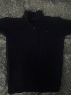 Mörkblå kabelstickad tröja Polo Ralph Lauren - Kabelstickad mörkblå tröja från Polo Ralph Lauren med halv dragkedja och liten röd logga broderad på bröstet. Tröjan har hög krage och är perfekt för lager-på-lager. Klassisk och tidlös design som funkar till det mesta. Kan gå ner i pris på en snabb affär