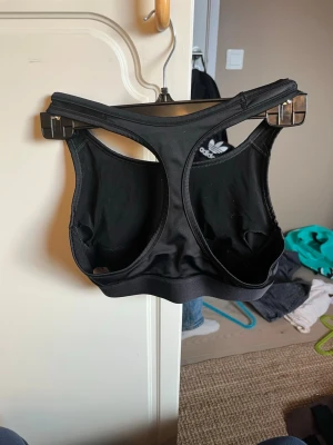 Svart sport-bh från Victoria Sport - Snygg svart sport-bh från Victoria Sport med bred resår under bysten och stor vit logga framtill. Bh:n har brottarrygg och är tillverkad i ett stretchigt material som passar perfekt för träning.