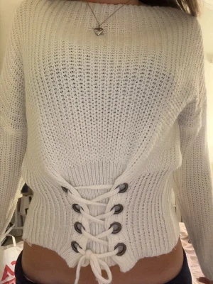 Vit stickad tröja med snörning - Trendig vit stickad tröja med breda ärmar och snygg snörning i midjan. Tröjan har en croppad passform och ribbstickade detaljer vid ärmslut och nederkant. Perfekt för dig som gillar en unik och cool look.💘