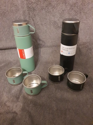Två termosar med fyra muggar - Säljer två termosar, en grön och en svart, båda med matchande muggar i metall och plast. Termosarna rymmer 500 ml och har praktiska lock som även fungerar som kopp. Perfekt för utflykter eller camping. Båda för 250 eller en för 170