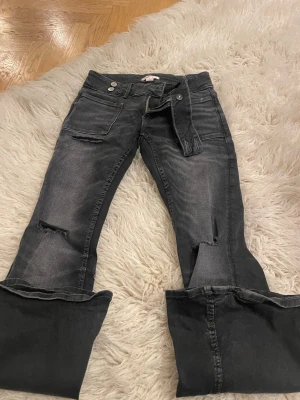 Svarta slitna jeans från Gina Tricot - Säljer ett par svarta jeans från Gina Tricot med slitningar på knäna och råa kanter vid bensluten. Jeansen har fickor, dragkedja och knappstängning. Perfekta för en avslappnad och trendig look. Aldrig använda, inga slitningar eller så. 