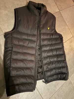 Svart vadderad väst från Lyle & Scott - Svart väst från Lyle & Scott med gul logga på bröstet.