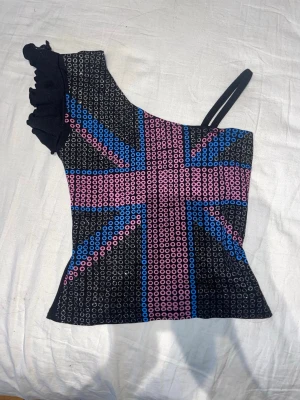 Söt glittrig off shoulder tröja  - Glittrig tröja med brittisk flagga motiv. Den är off shoulder med ena ärmen som ett linne och andra ruffles. Köpt second hand men mycket bra skick. Skriv för prisförslag eller fler bilder💕